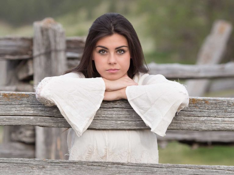 A young women leaning on a fence post.